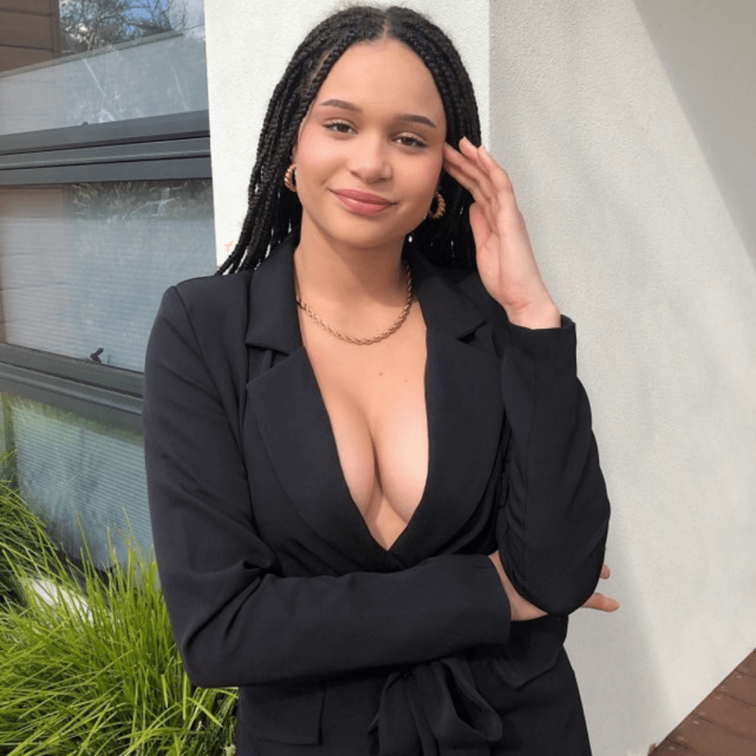 girl in braids in black blazer dress using black boob tape for boob lift wearing gold hoop earrings