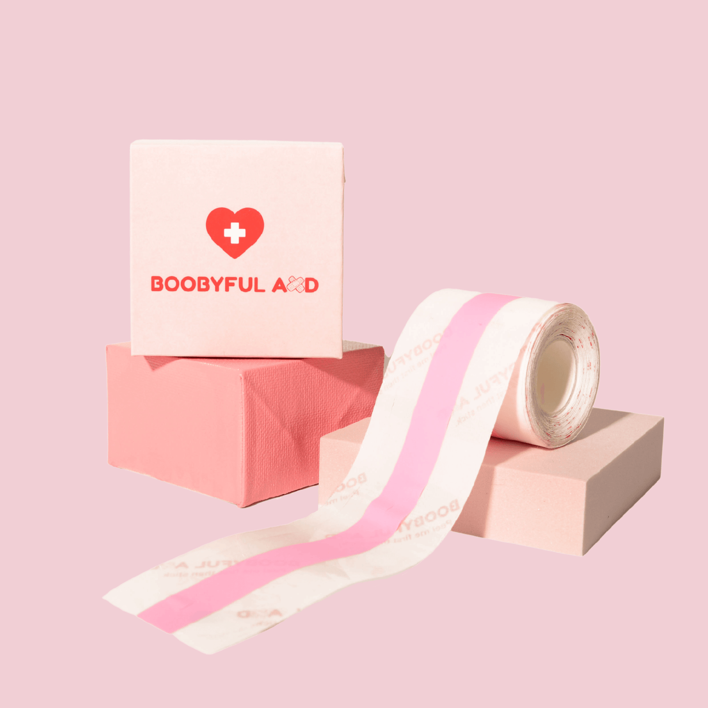boobyful aid clear boob tape on pink cube stands and boobyful aid box packaging